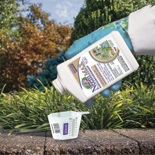 A gloved hand pours Captain Jack’s® Neem Max Concentrate into a clear measuring cup outdoors, surrounded by green plants—ideal for organic gardening and natural pest control when used with other organic products.