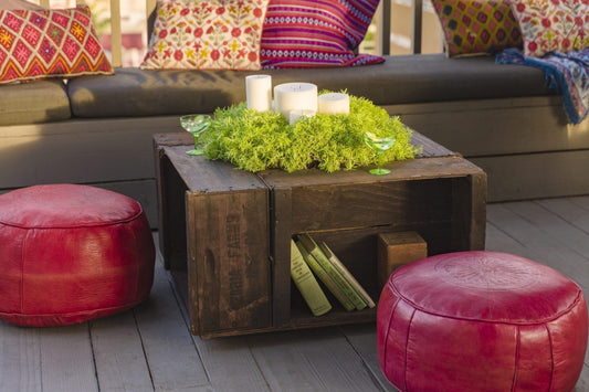 A wood table with a planter in the center next to two red cushions on a wood deck.