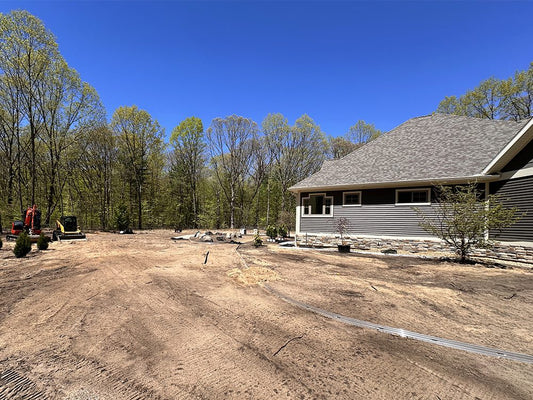 House under construction with a clear blue sky, no grass, and trees in the background