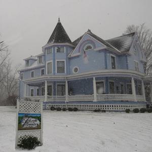 Large, light blue victorian style house with white trim and three stories with a snow covered front yard