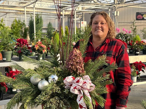 Woman in flannel standing behind a winter wreath adorned with dried hydrangea blooms