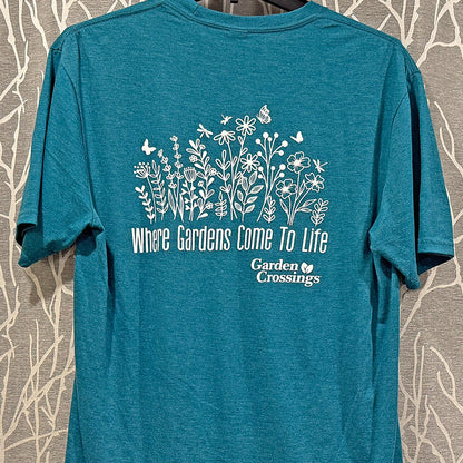 The Garden Crossings Tshirt is a teal unisex shirt with white flower, butterfly, and bee illustrations. Featuring "Where Gardens Come To Life" above the logo and a small heart, it’s perfect for fans of unique gardening t-shirts. - 