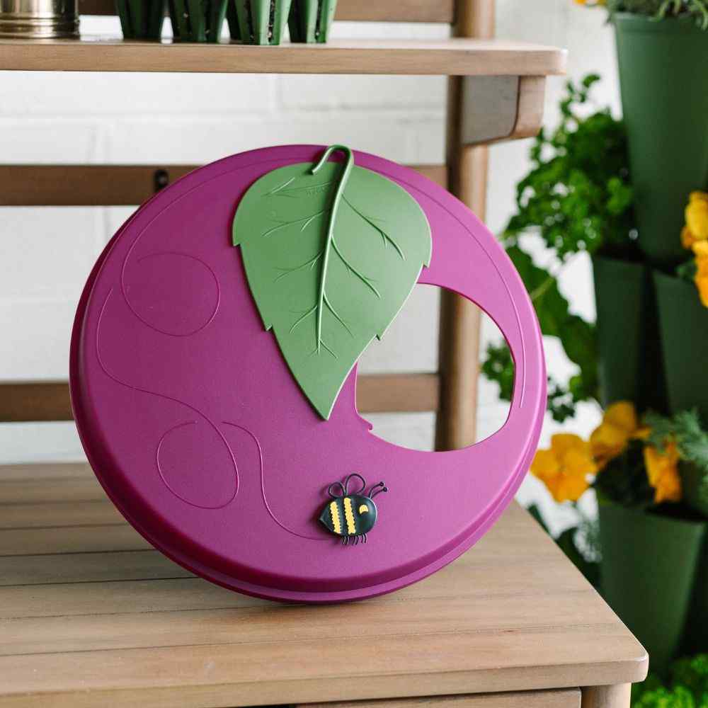 Purple circular object with green leaf and bee design on a wooden surface. - 
