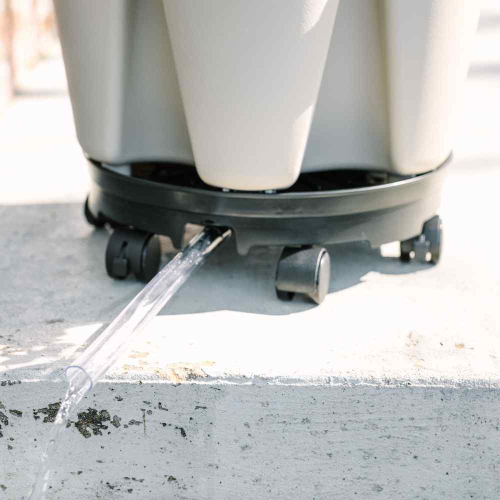 White container on a black base with wheels, a clear tub draining water from beneath the base - 